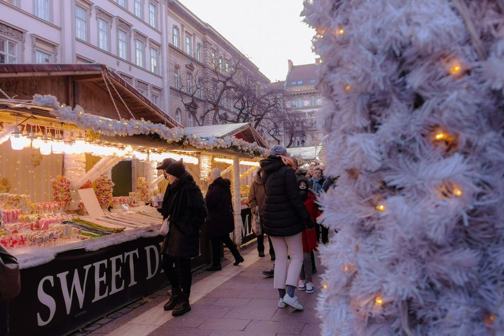 Budapester Weihnachtsmarkt am Nachmittag mit Ständen, Lichterketten und einem weißen Lichterbaum, Familien beim Bummeln