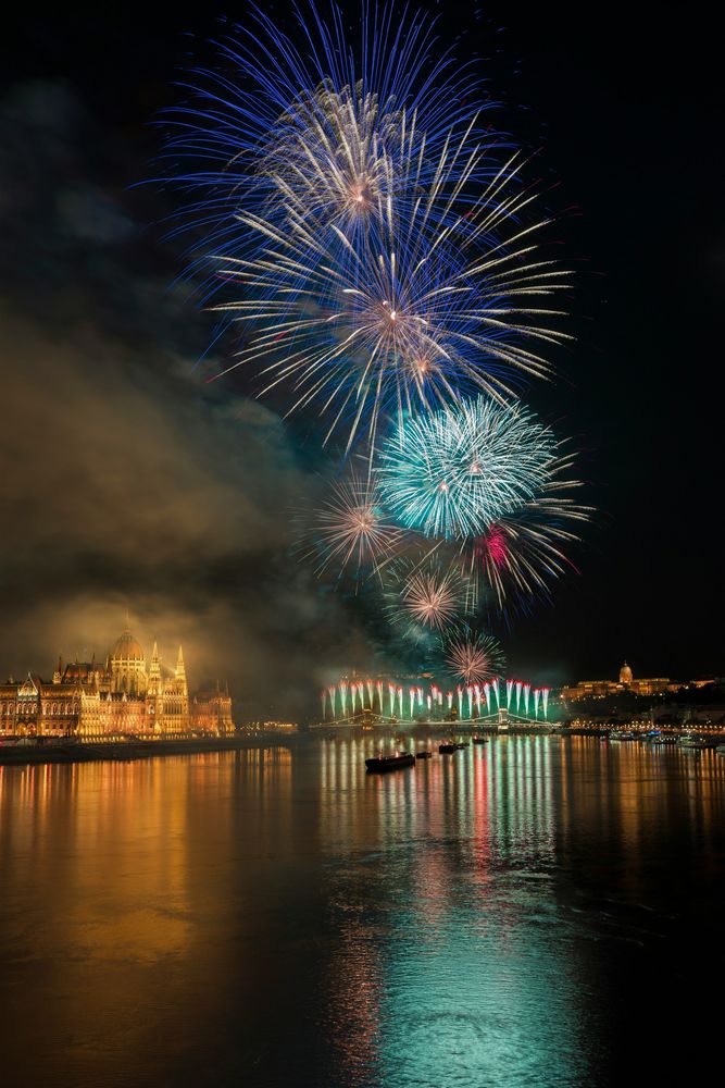 Blau-grünes Feuerwerk über der Donau in Budapest, links das beleuchtete Parlament, rechts der Burgberg