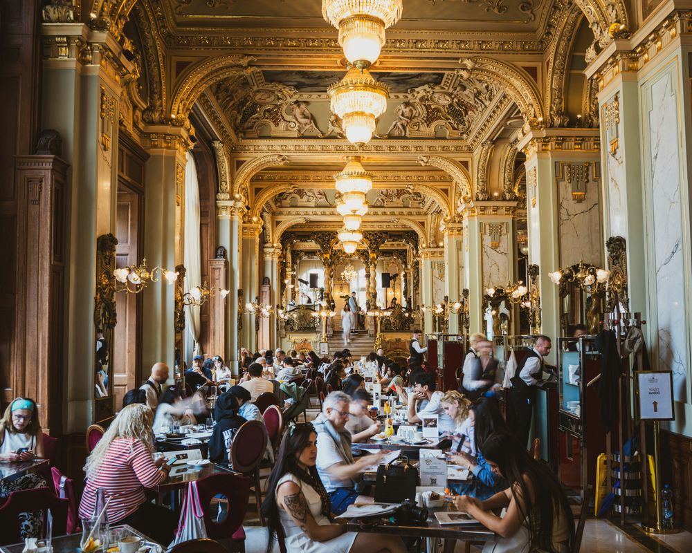 Der prunkvolle Innenraum des New York Café in Budapest mit Kronleuchtern, Goldstuck und besetzten Tischen