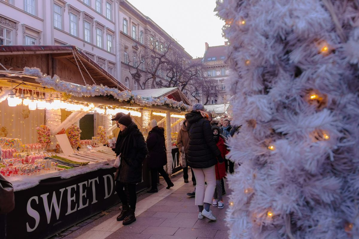 Budapester Weihnachtsmarkt am Nachmittag mit Ständen, Lichterketten und einem weißen Lichterbaum, Familien beim Bummeln