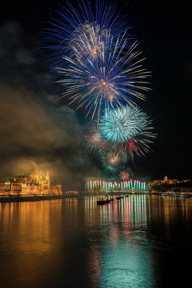 Blau-grünes Feuerwerk über der Donau in Budapest, links das beleuchtete Parlament, rechts der Burgberg
